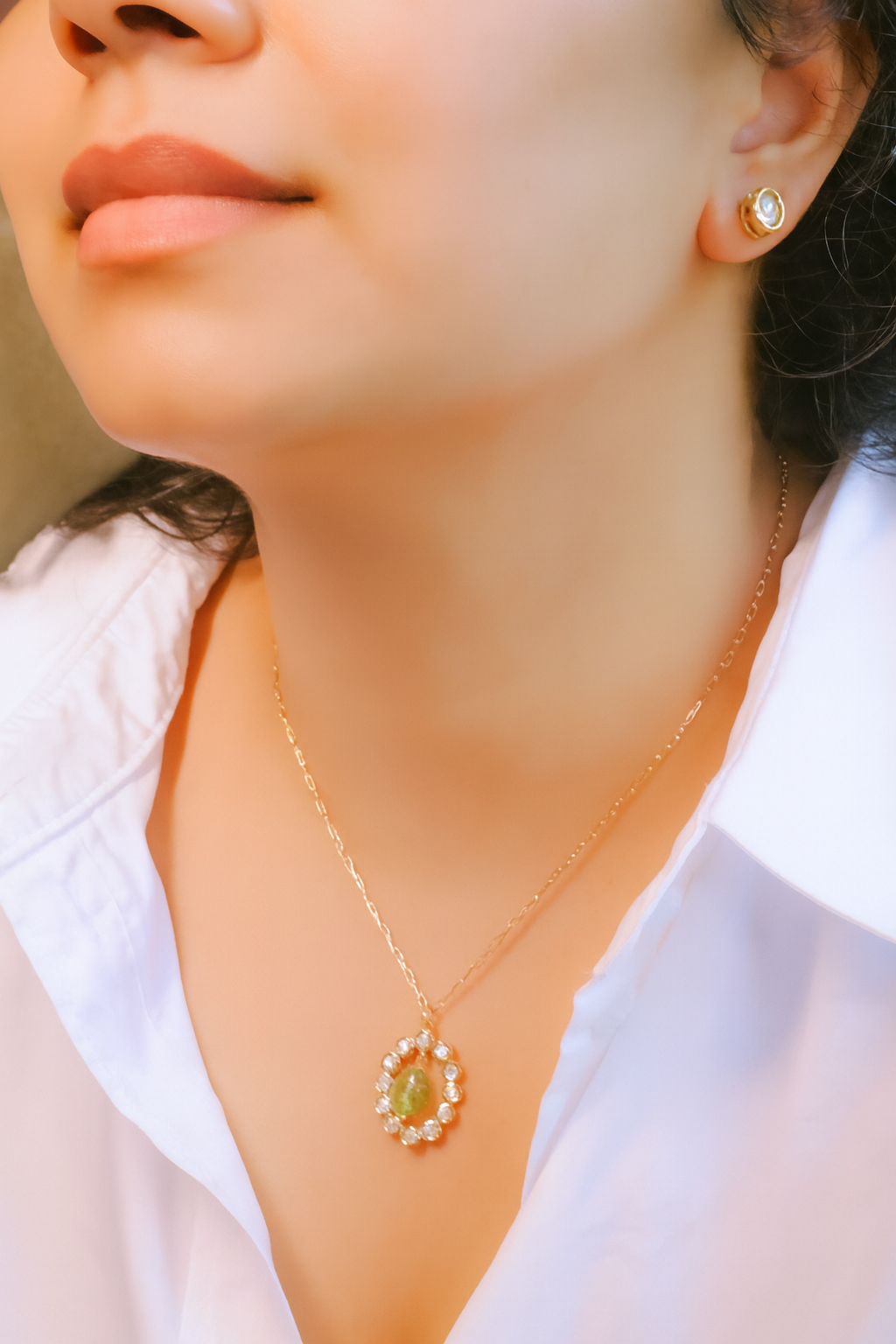 Close-up of a person wearing a gold necklace with a green pendant and matching earrings.