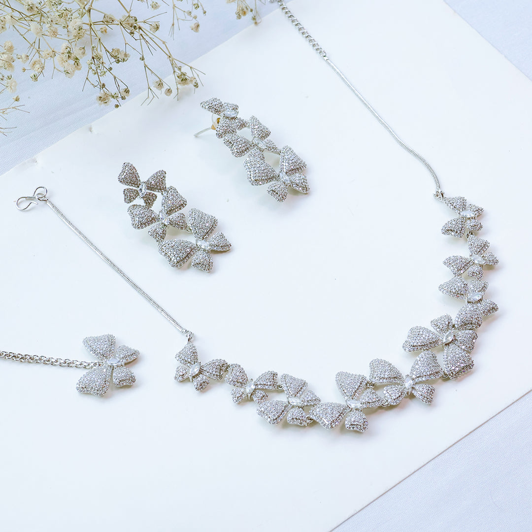Silver jewelry set with necklace and earrings on a white surface with flowers.