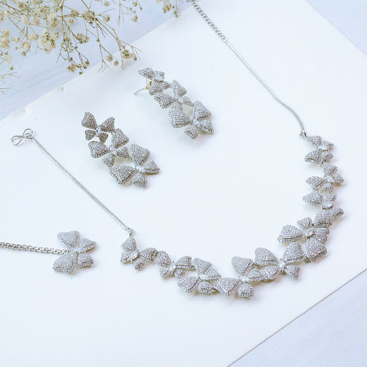 Silver jewelry set with necklace and earrings on a white surface with flowers.