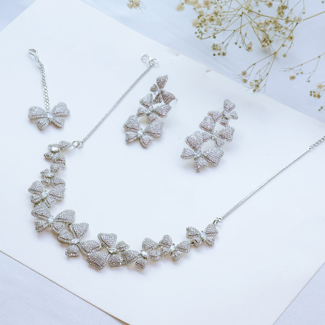 Silver necklace and earrings set on a white surface with dried flowers.