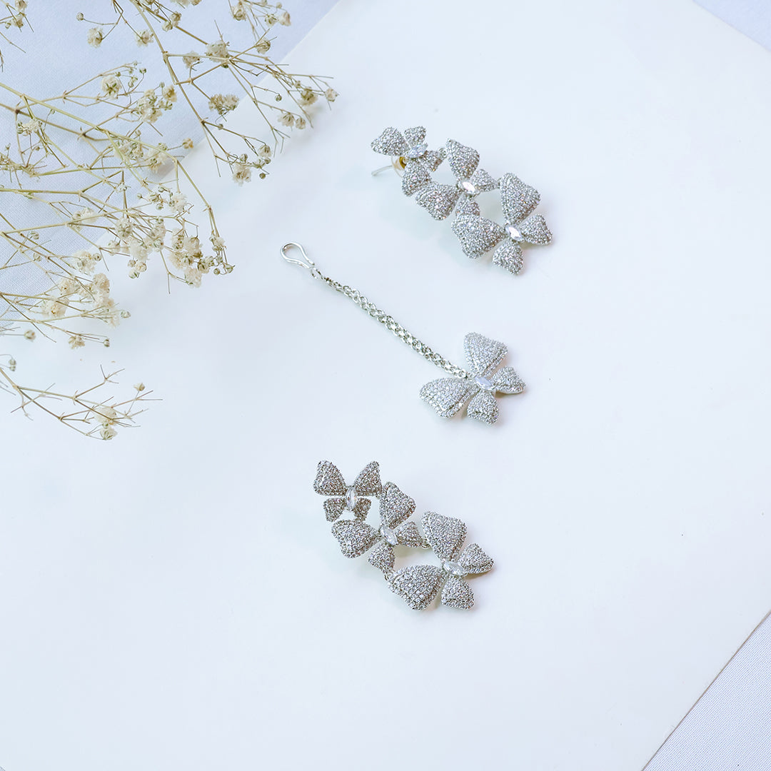 Silver bow-shaped earrings on a light blue background with dried flowers.