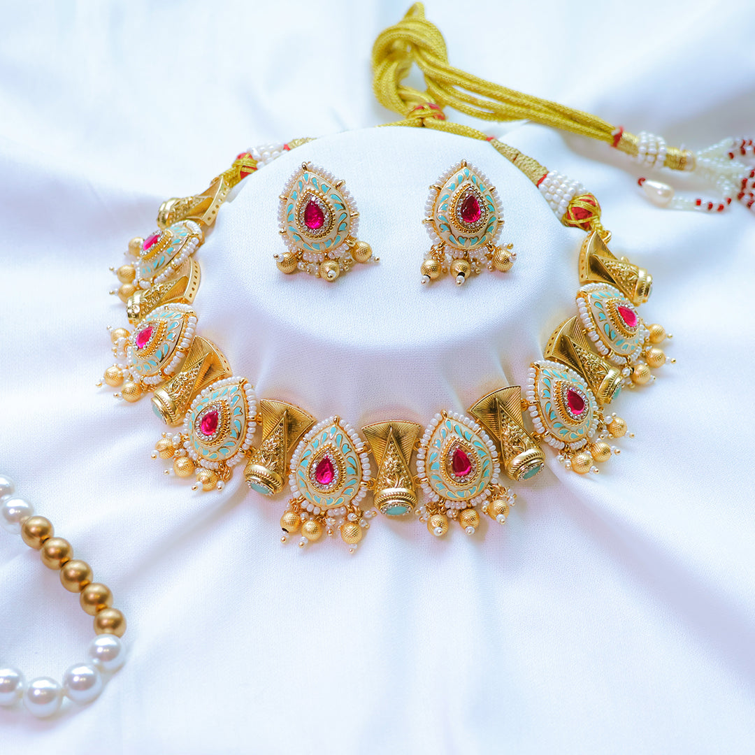 Gold jewelry set with red and green stones on a white background