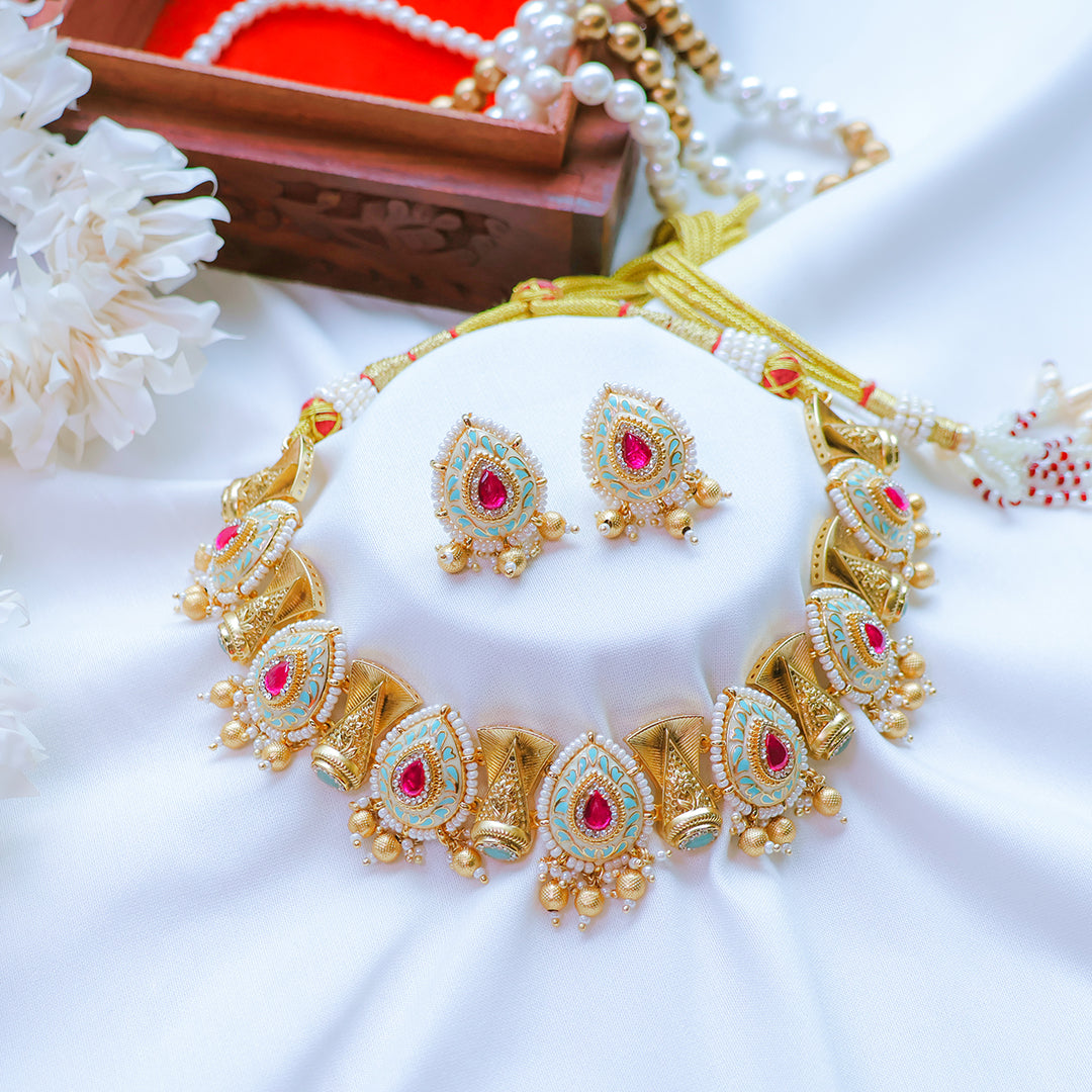 Gold necklace with red and green stones on a white surface