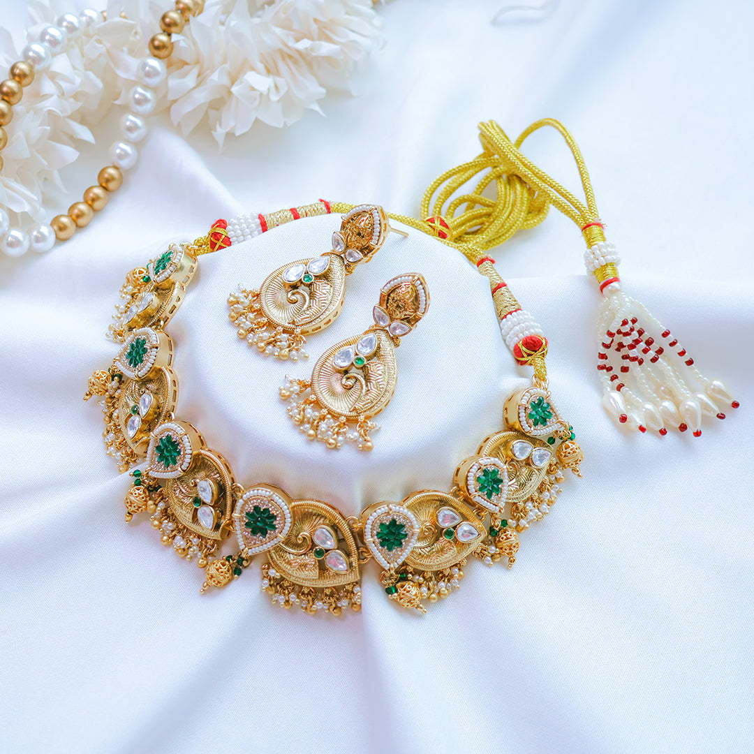Gold necklace with green gemstones and matching earrings on a white background