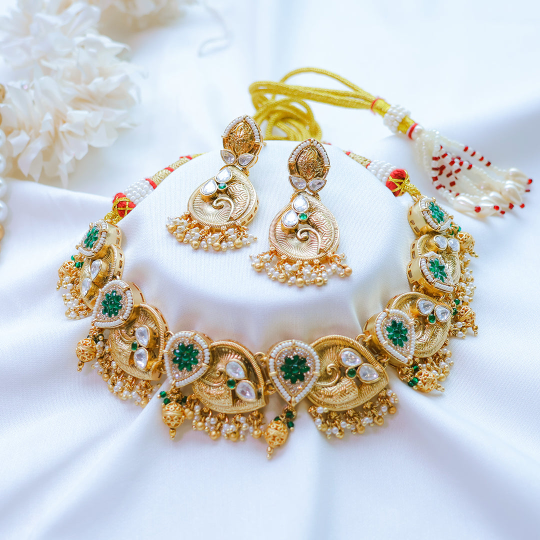Gold necklace and earrings set with green gemstones on a white fabric background