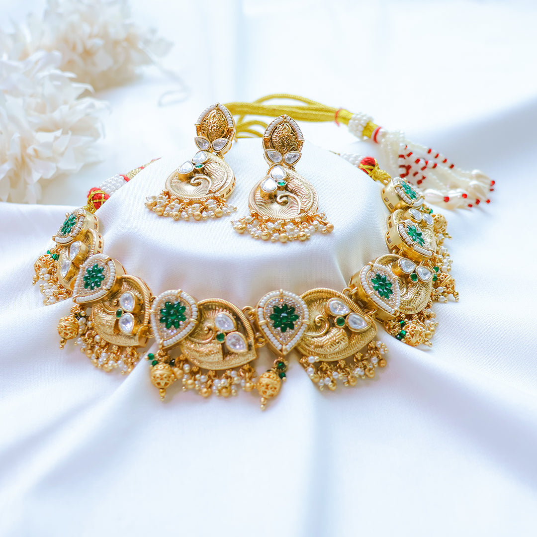 Gold necklace and earrings with green gemstones on a white fabric background