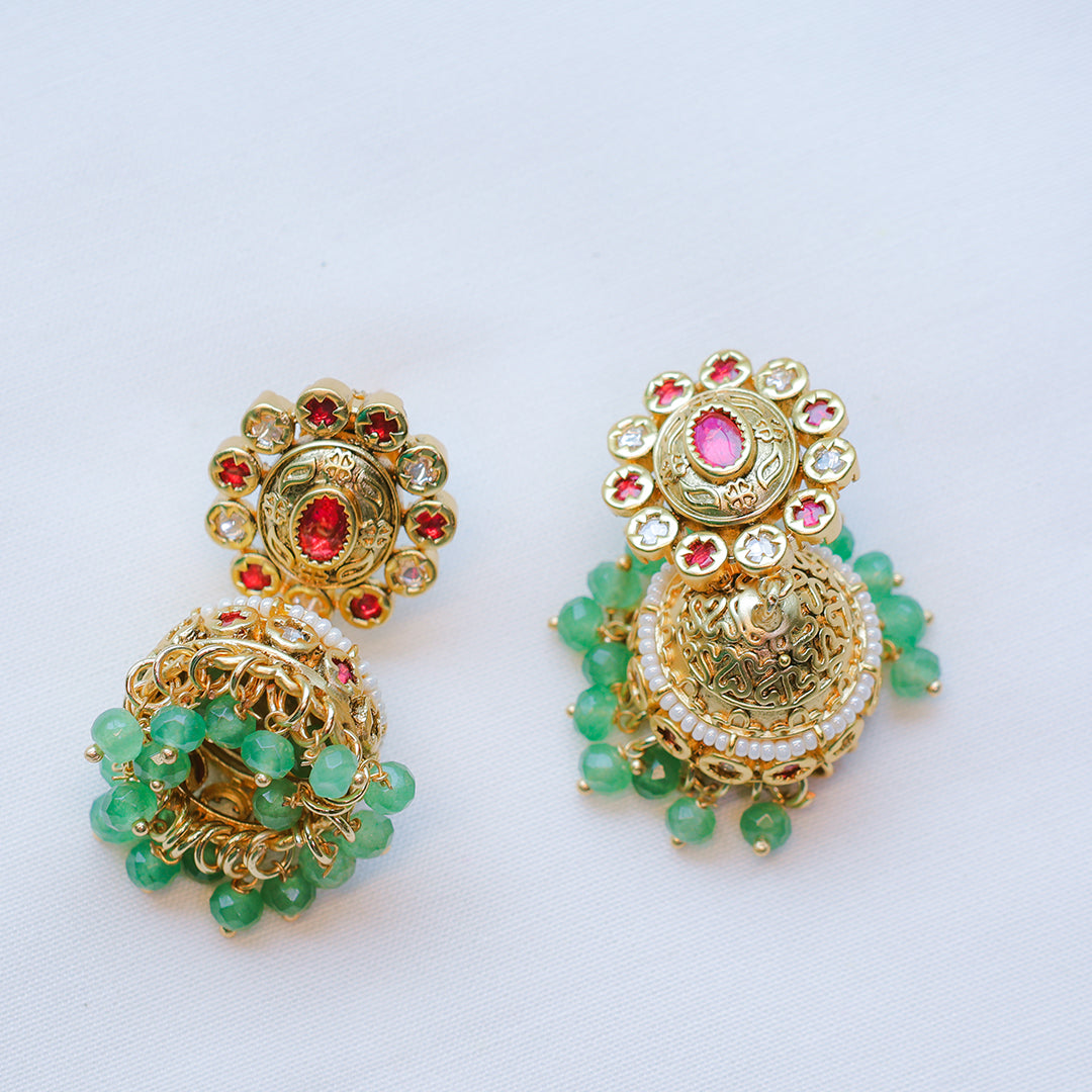 Gold earrings with green beads and red stones on a white background