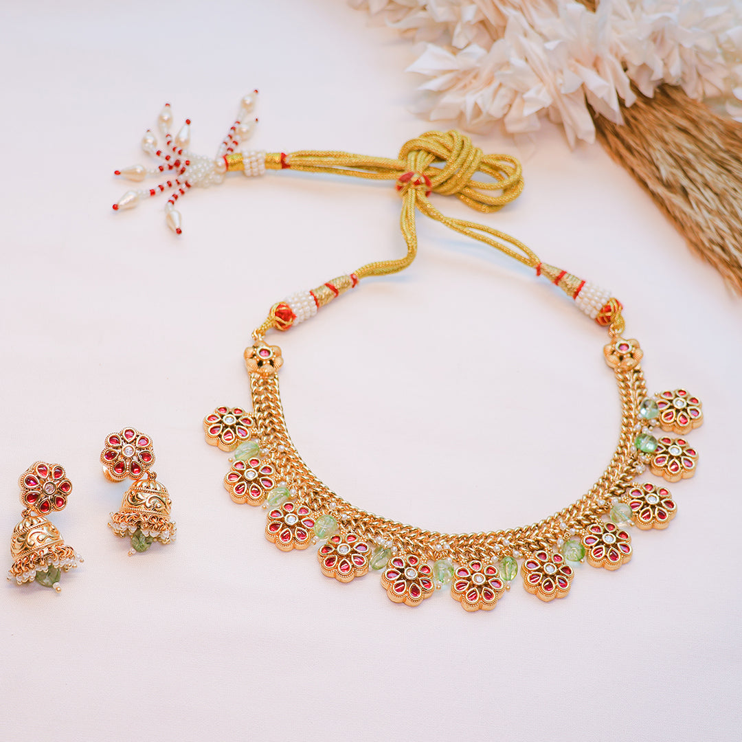 Gold necklace with floral designs and matching earrings on a light background