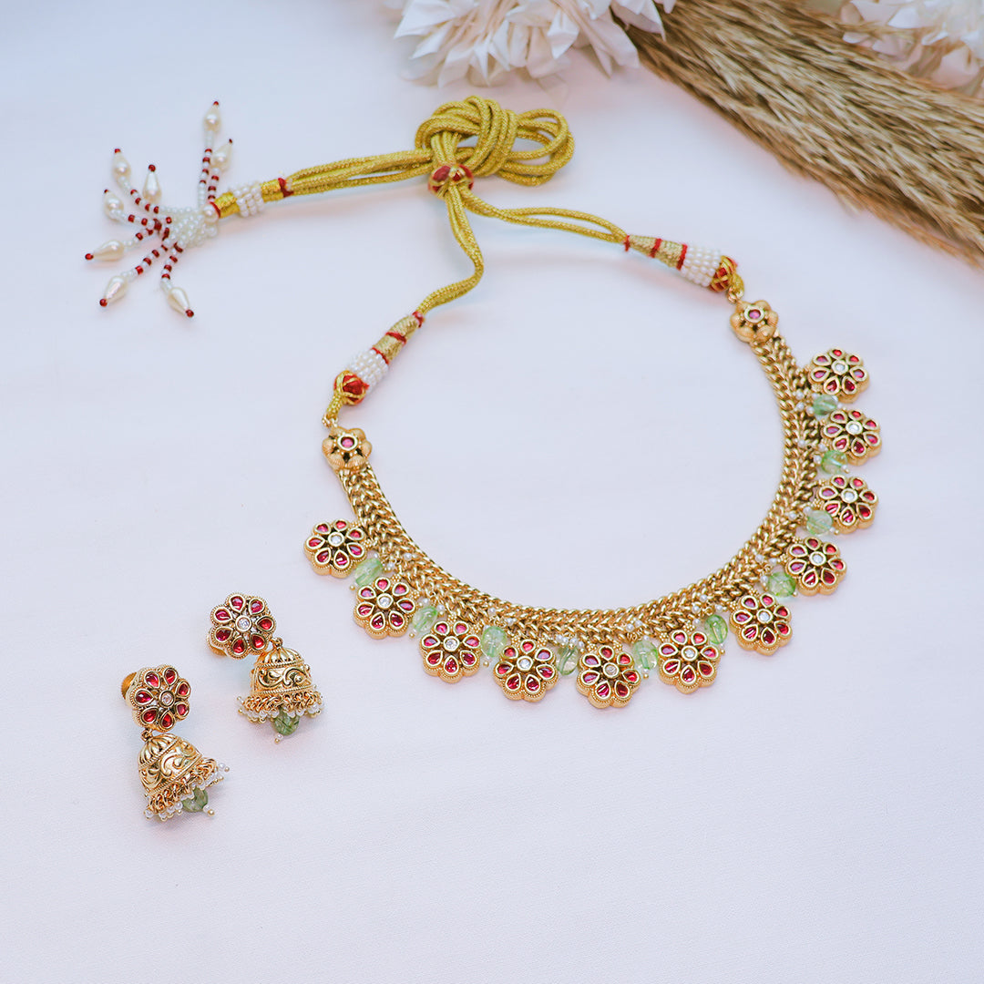 Gold necklace with floral designs and matching earrings on a light background