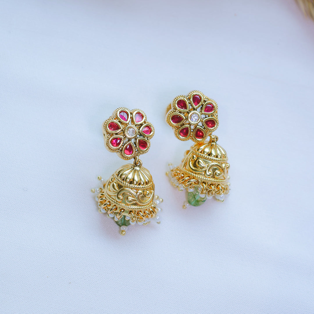 Gold earrings with red and green gemstones on a light blue background