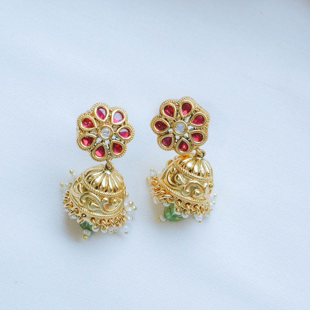 Gold earrings with red gemstones on a light gray background