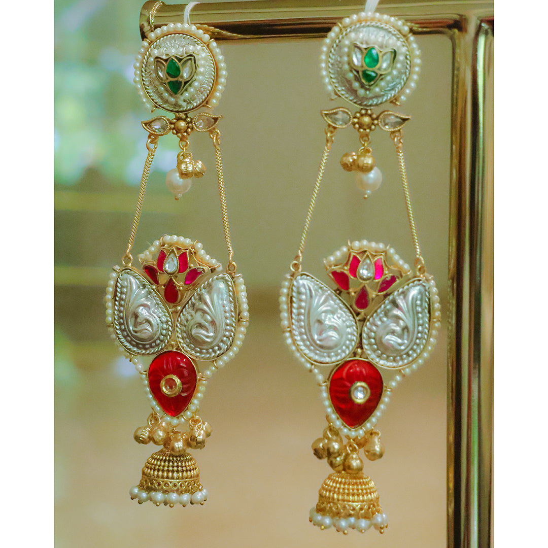 Ornate earrings with red and gold details on a reflective surface