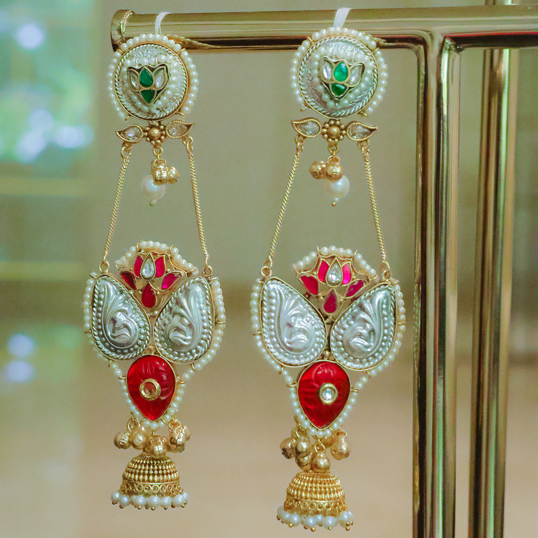 Ornate earrings with red and gold design on a stand