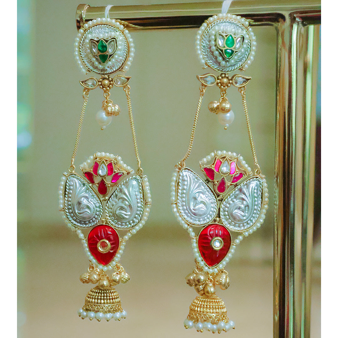 Ornate earrings with red, gold, and pearl details on a reflective surface.