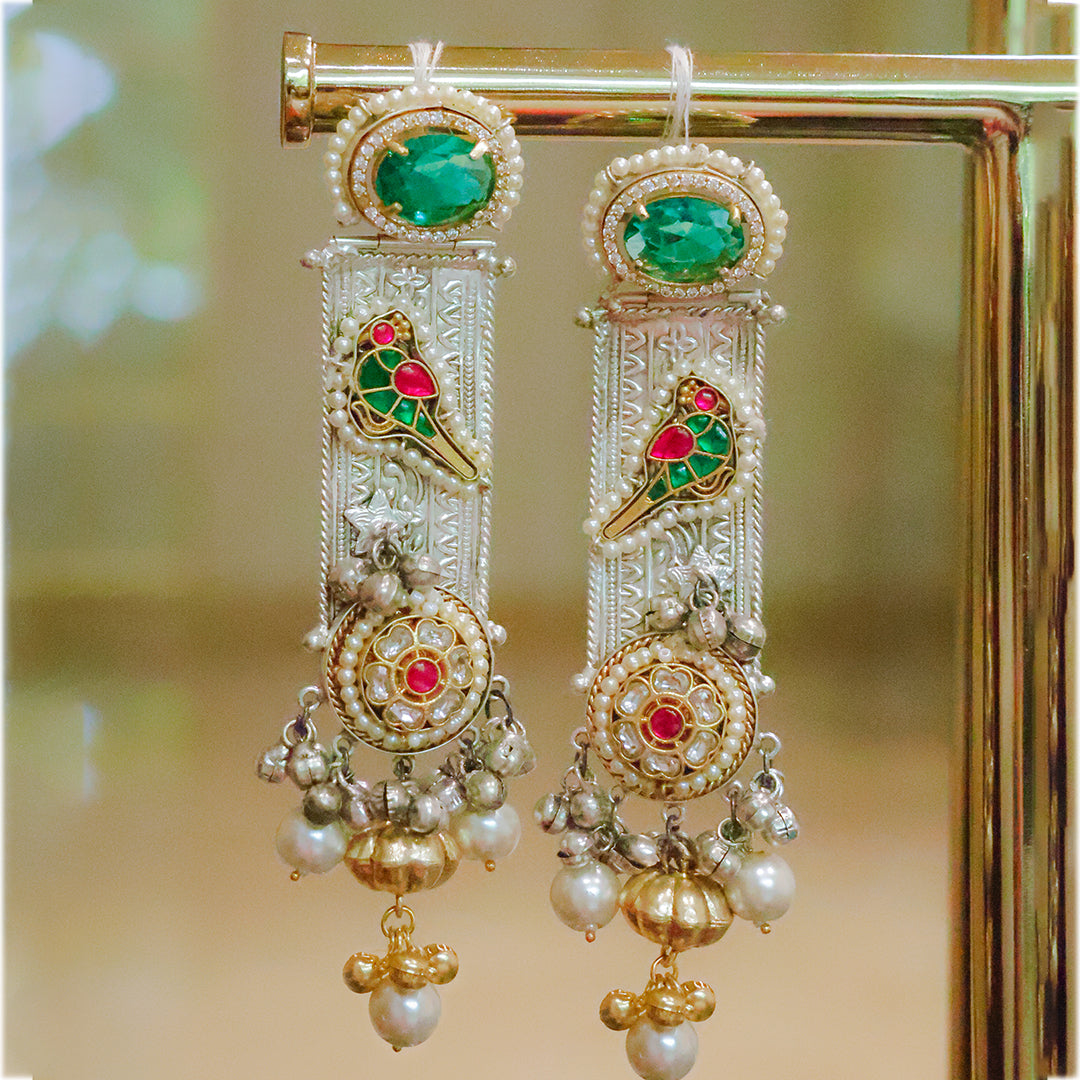 Ornate earrings with green, red, and gold colors on a stand.