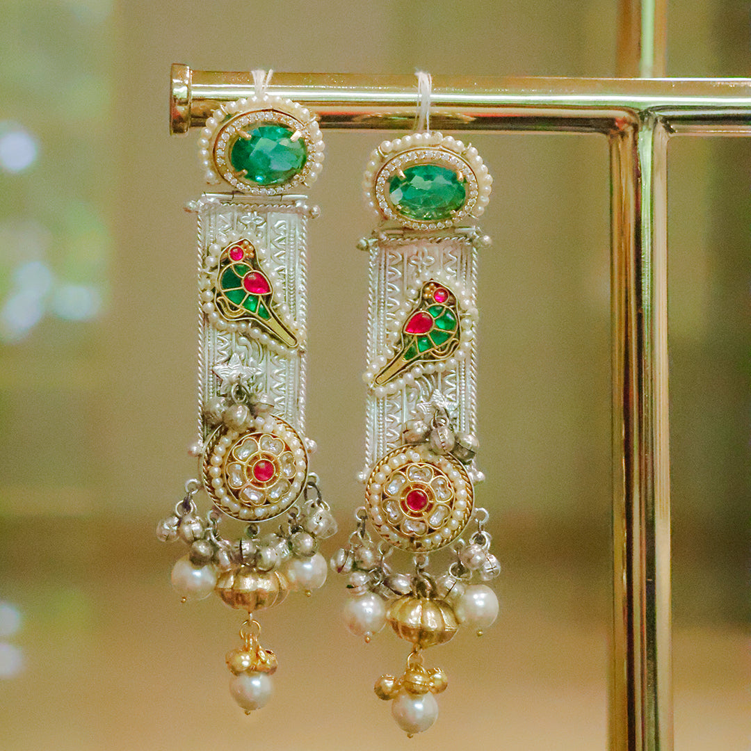 Ornate earrings with green gemstones and pearl-like beads on a gold stand.