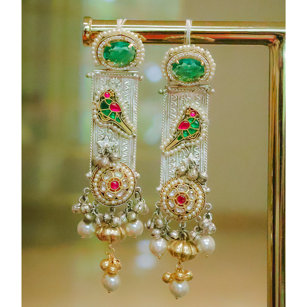 Ornate earrings with green, red, and gold colors on a reflective surface.