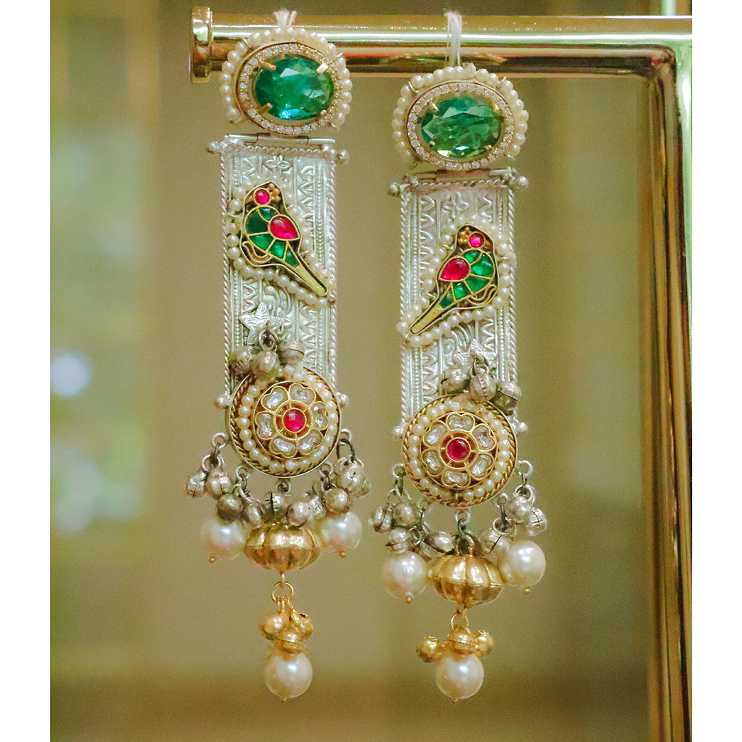 Ornate gold earrings with green and red gemstones on a blurred background