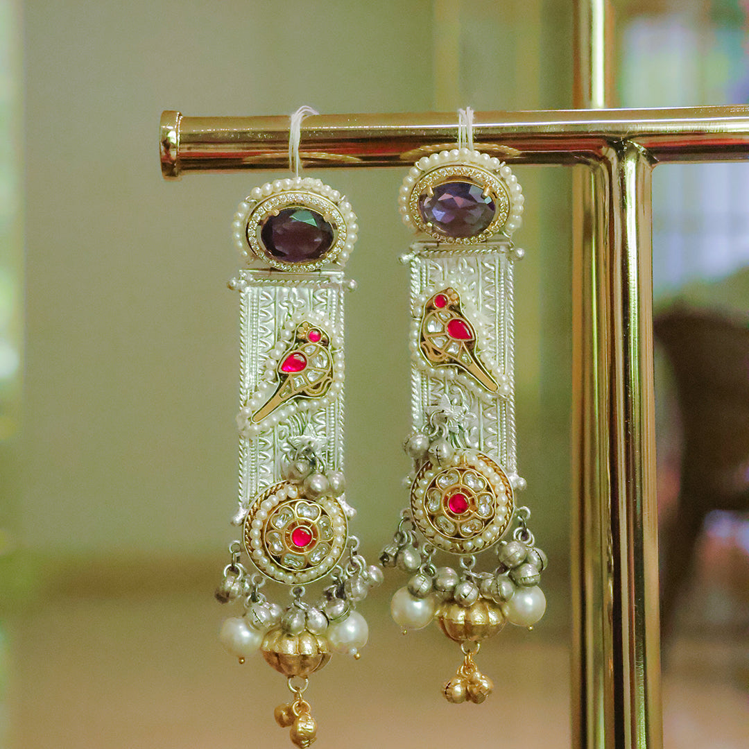 Ornate gold earrings with red gemstones and pearl-like beads on a stand.