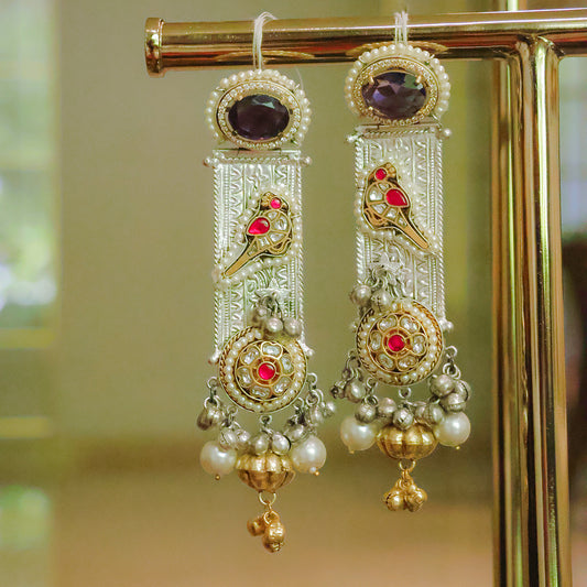 Ornate earrings with gold and red accents on a stand against a blurred background