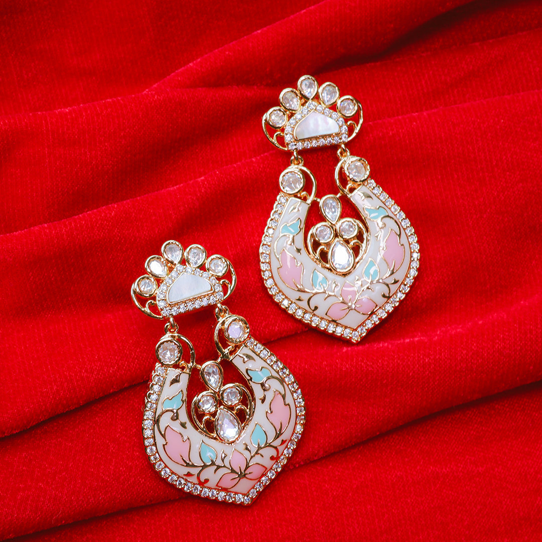 Ornate earrings with pink and gold details on a red fabric background