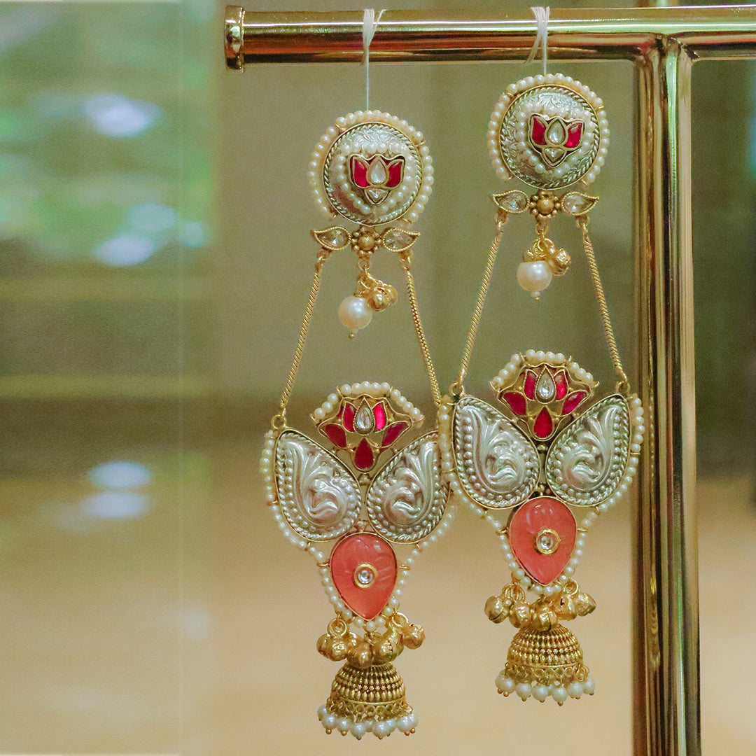 Ornate earrings with red and gold design on a reflective surface