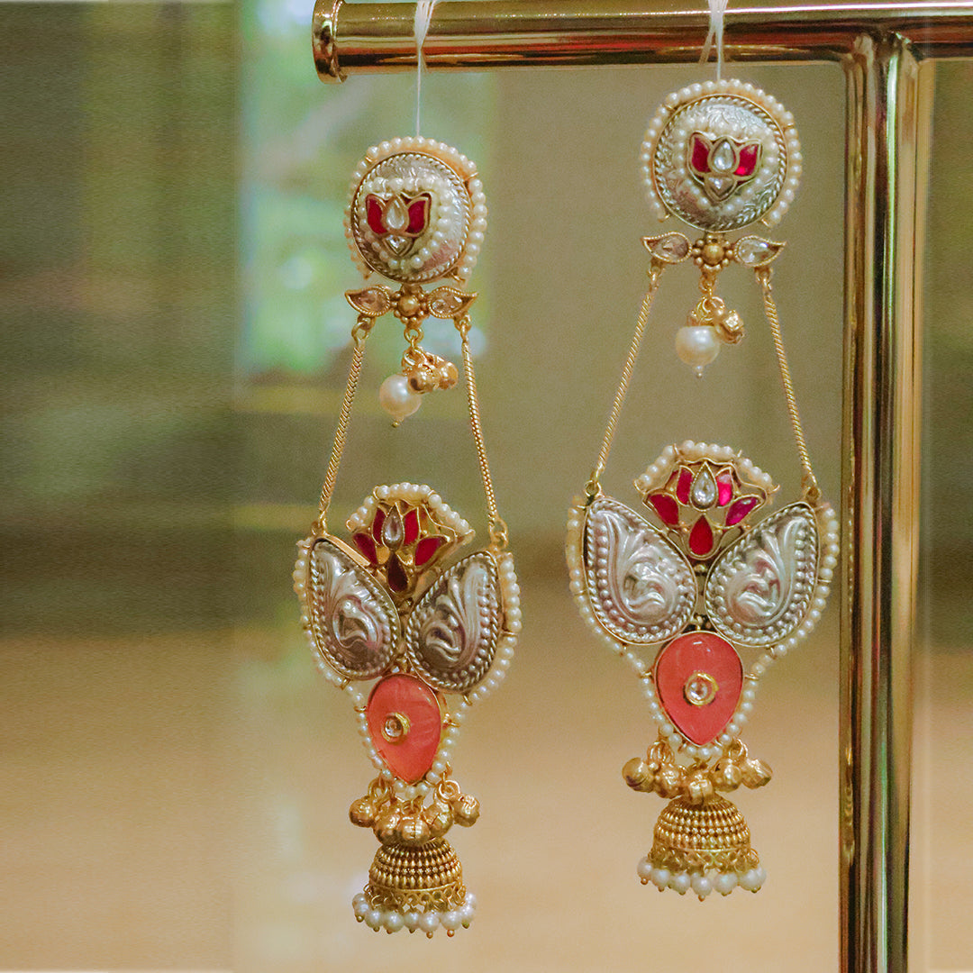 Ornate earrings with gold, red, and pearl details on a reflective surface.