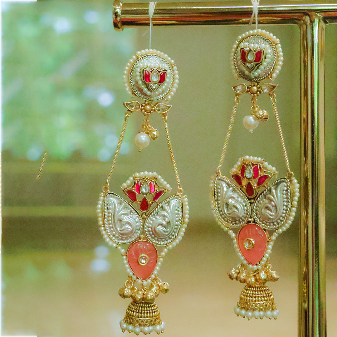 Decorative earrings with gold, red, and pearl details on a blurred green background