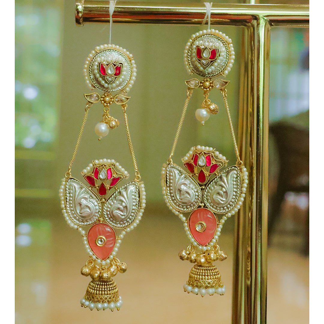 Ornate earrings with gold, red, and pearl details hanging against a blurred background.