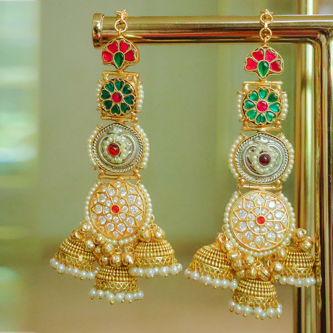 Gold earrings with red and green gemstones on a reflective surface