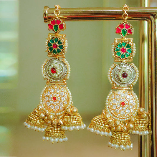 Gold earrings with red and green gemstones on a reflective surface