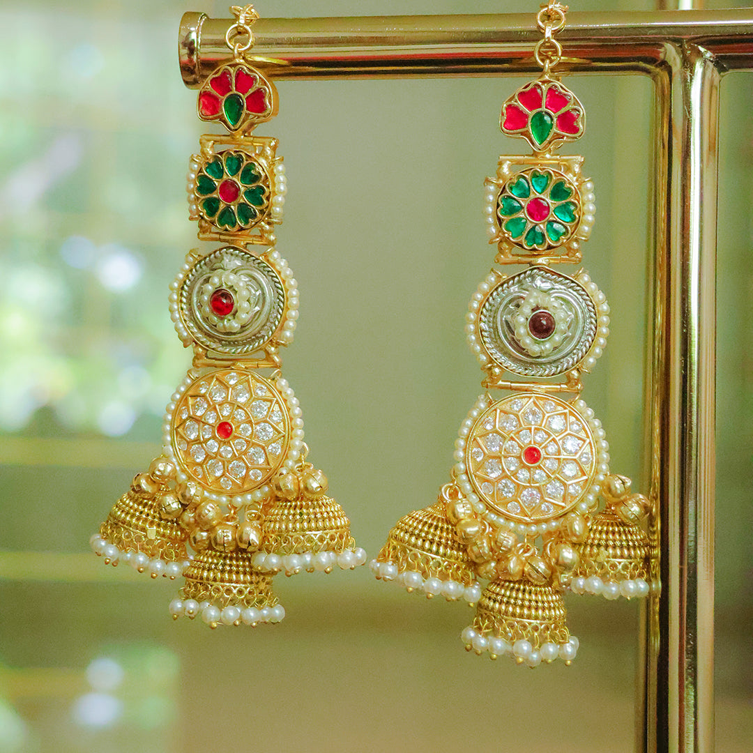 Gold earrings with green and red stones on a reflective surface