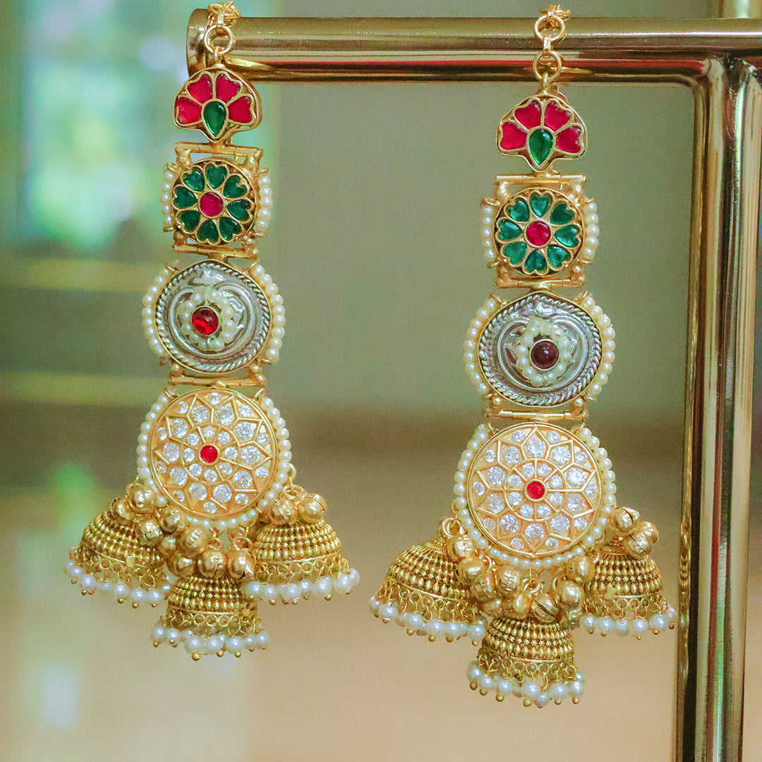 Ornate gold earrings with red and green gemstones on a stand.