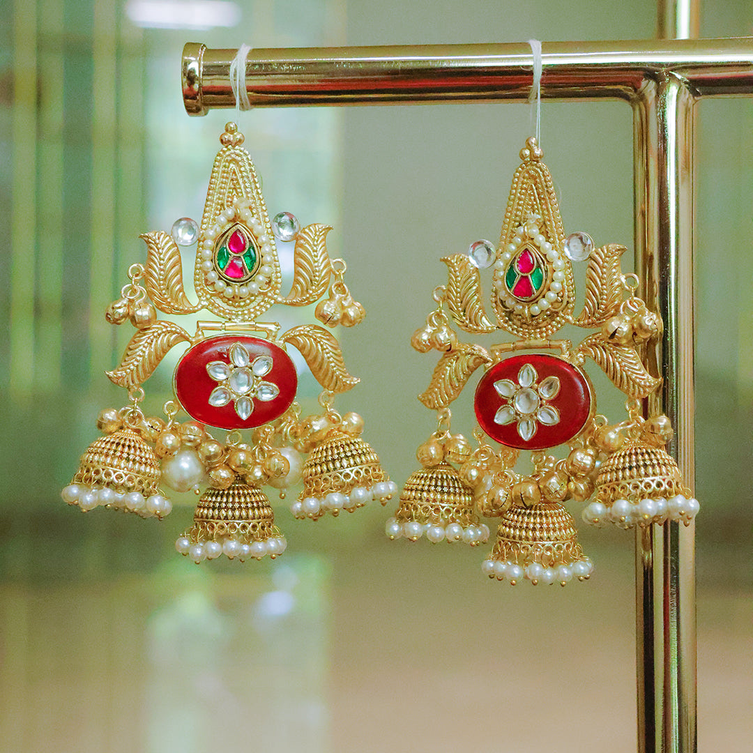 Ornate gold earrings with red center and pearl accents on a gold stand.