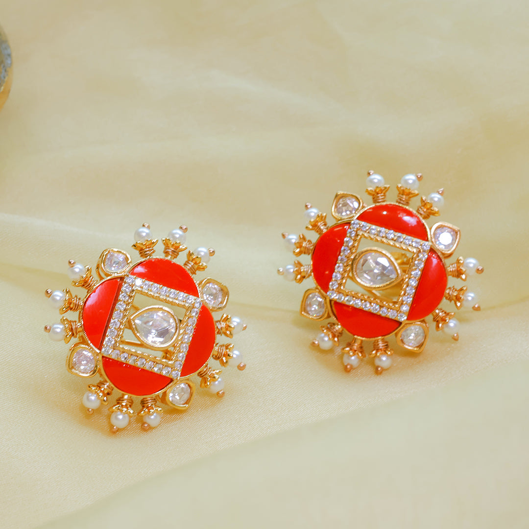 Ornate earrings with red center, gold frame, and pearl accents on a beige background