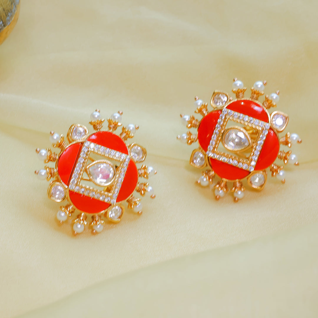 Pair of earrings with red center, gold frame, and pearl accents on a beige background