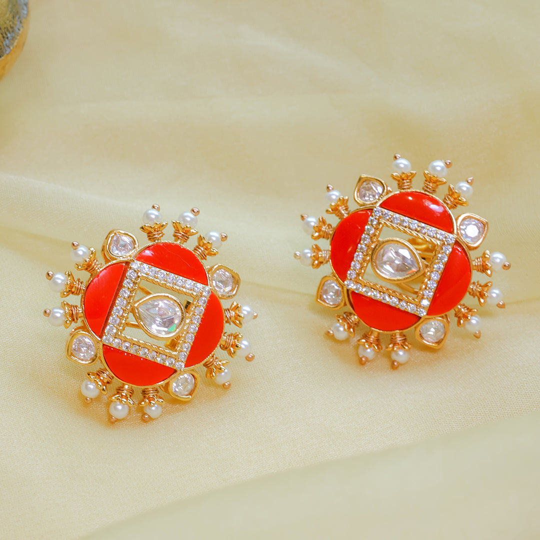 Pair of ornate earrings with red centers, gold frames, and pearl accents on a beige background.