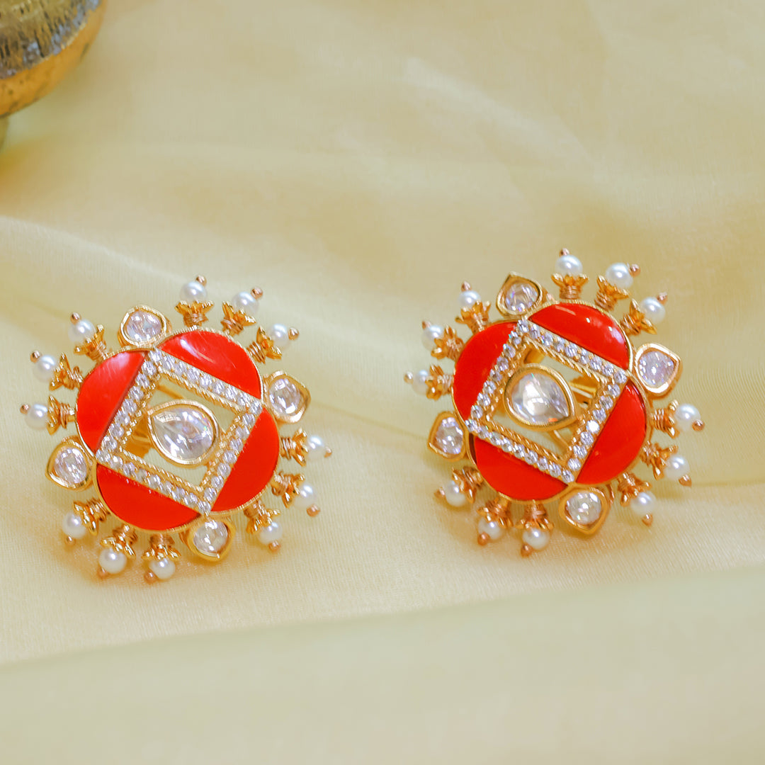 Pair of red earrings with gold and pearl accents on a beige background