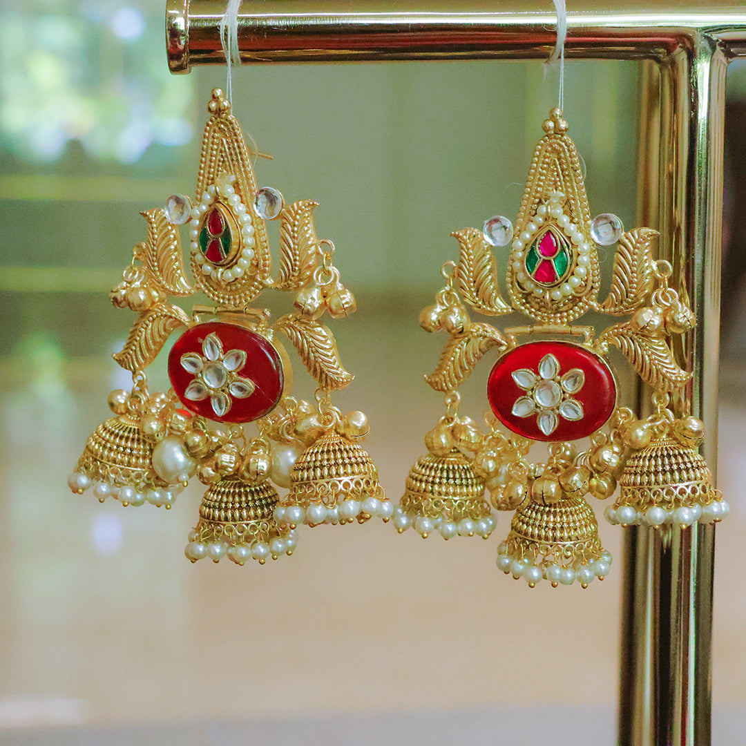 Gold earrings with red and pearl details on a stand