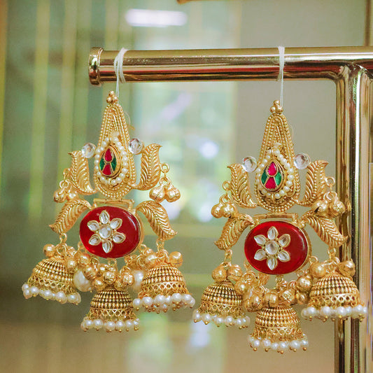 Gold and red earrings with pearl details on a reflective surface