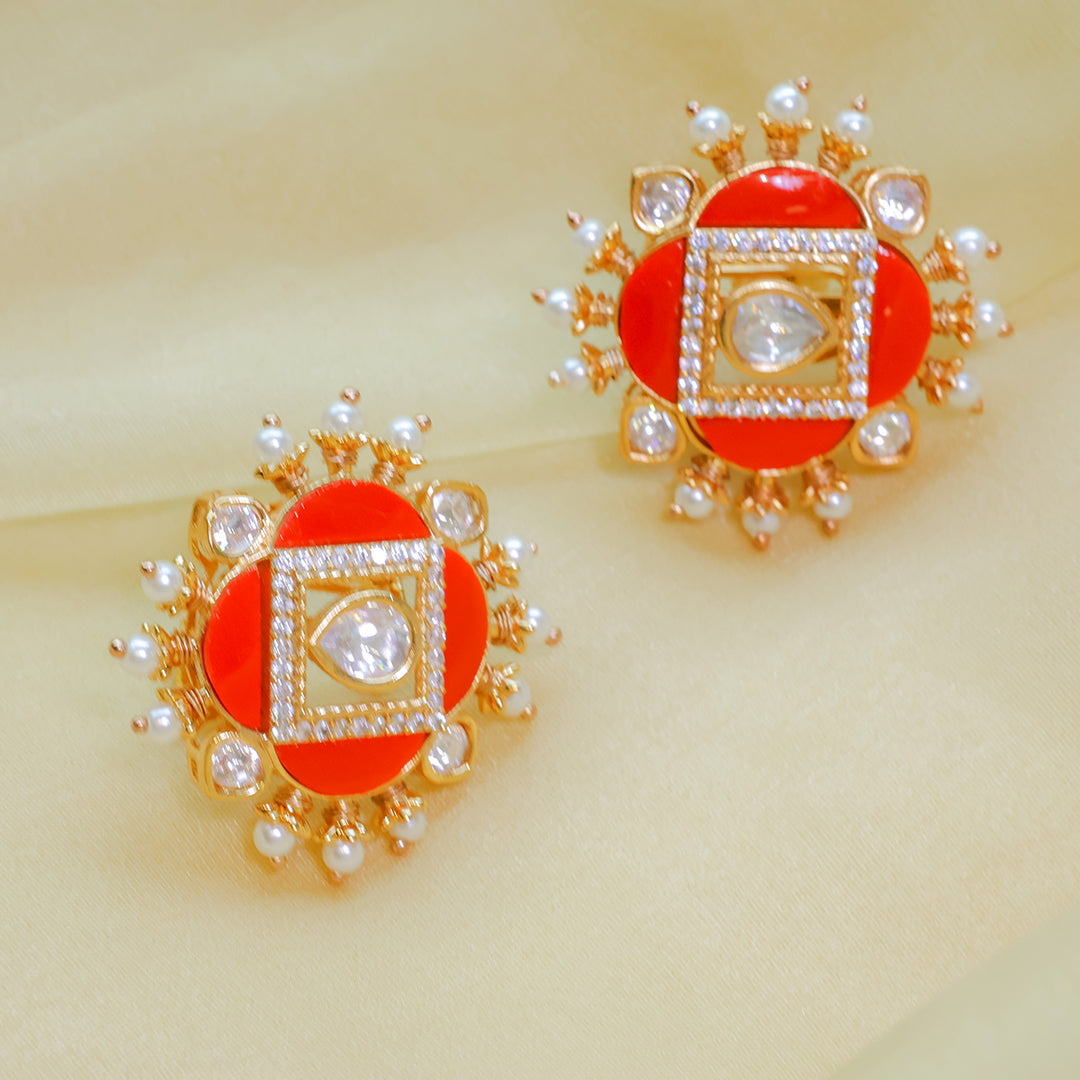 Pair of earrings with red centers, gold frames, and pearl accents on a beige background