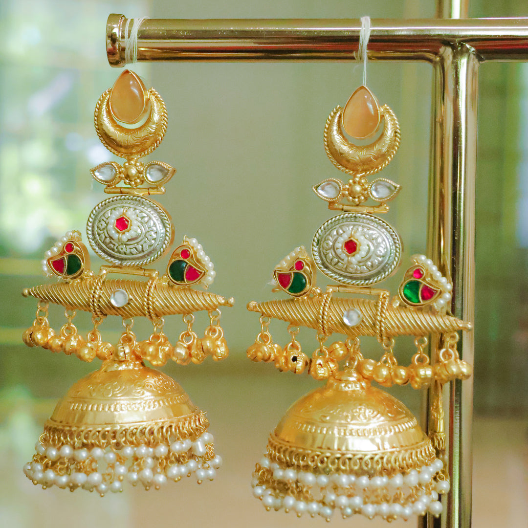 Gold earrings with intricate designs and pearl accents on a gold stand.