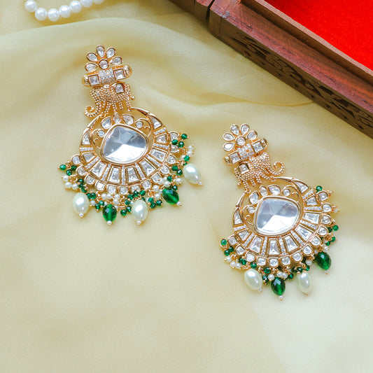 Pair of gold earrings with green and pearl accents on a beige fabric background