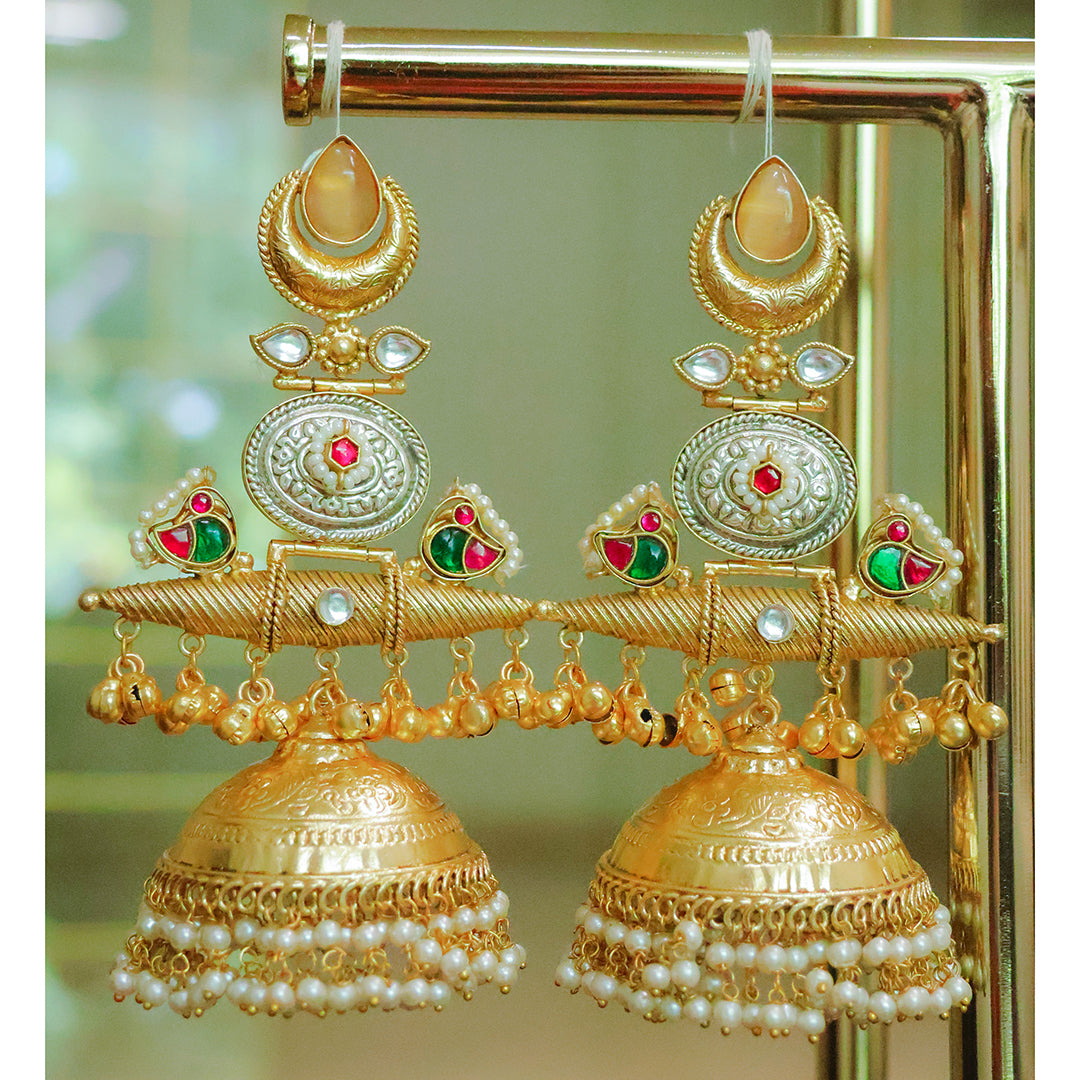 Gold earrings with intricate designs and pearl accents on a stand.
