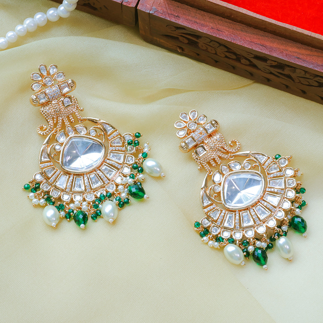 Ornate gold earrings with green and pearl accents on a light yellow surface.