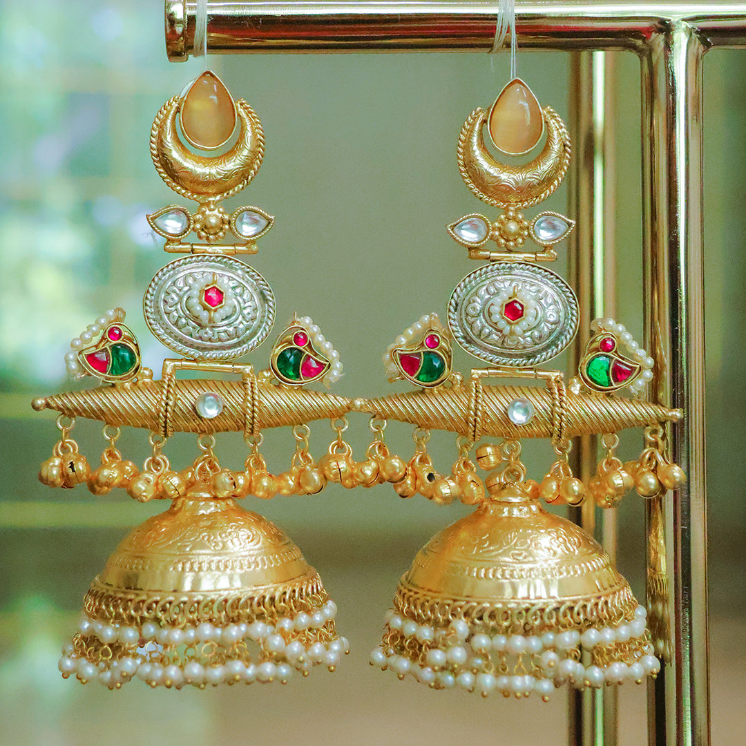 Ornate gold earrings with pearls and gemstones on a stand.
