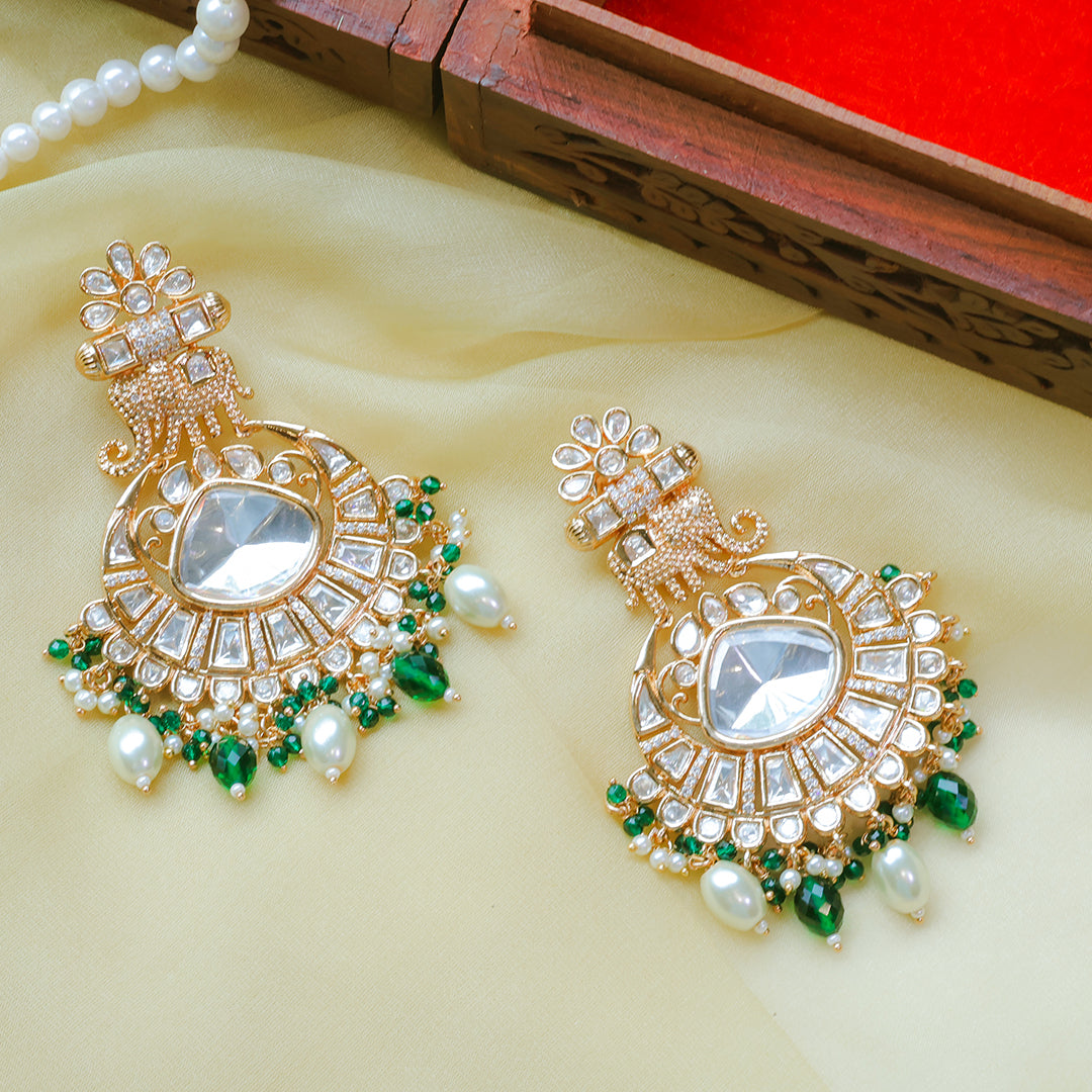 Pair of ornate gold earrings with pearls and green stones on a beige surface.