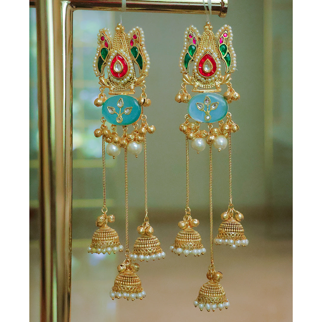Ornate gold earrings with colorful stones and pearl accents on a reflective surface.