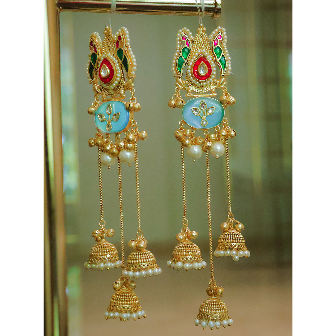 Ornate gold earrings with pearls and colorful stones on a reflective surface.