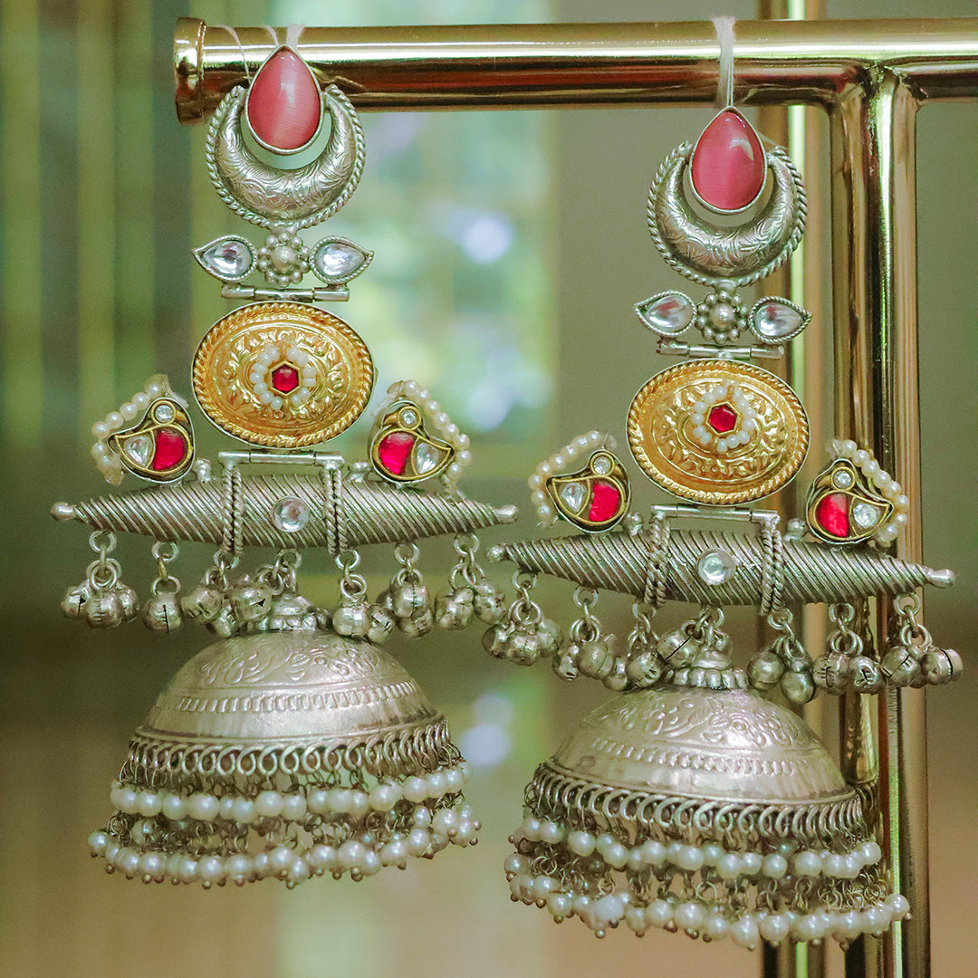 Ornate earrings with red stones and pearl details on a gold stand.